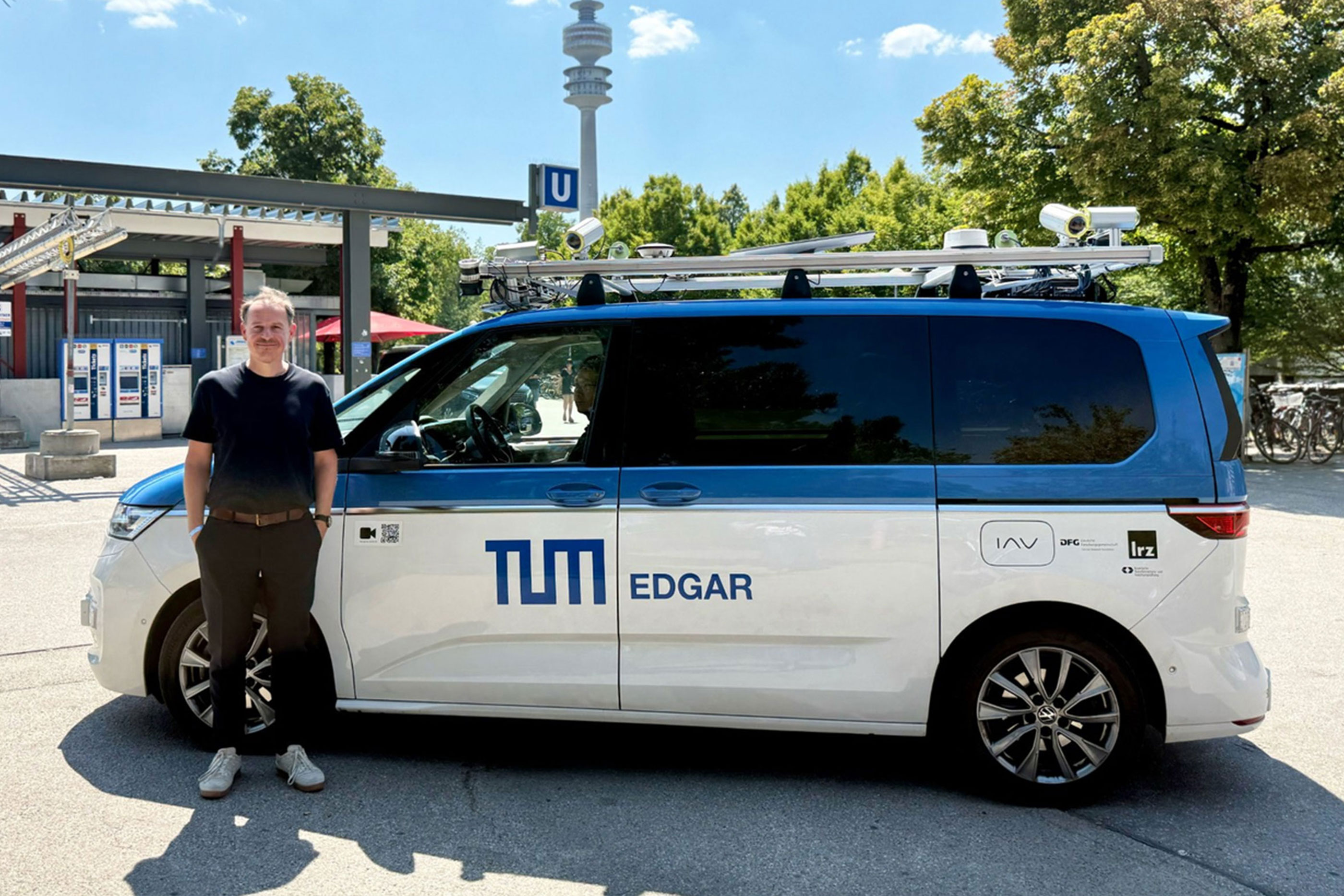 Mann steht vor einem Fahrzeug mit der Aufschrift TUM Edgar. Im Hintergrund der Olympiaturm