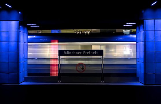 Fahrende U-Bahn im Münchner U-Bahnhof mit Beschilderung „Münchner Freiheit“ in der Mitte des Bildes